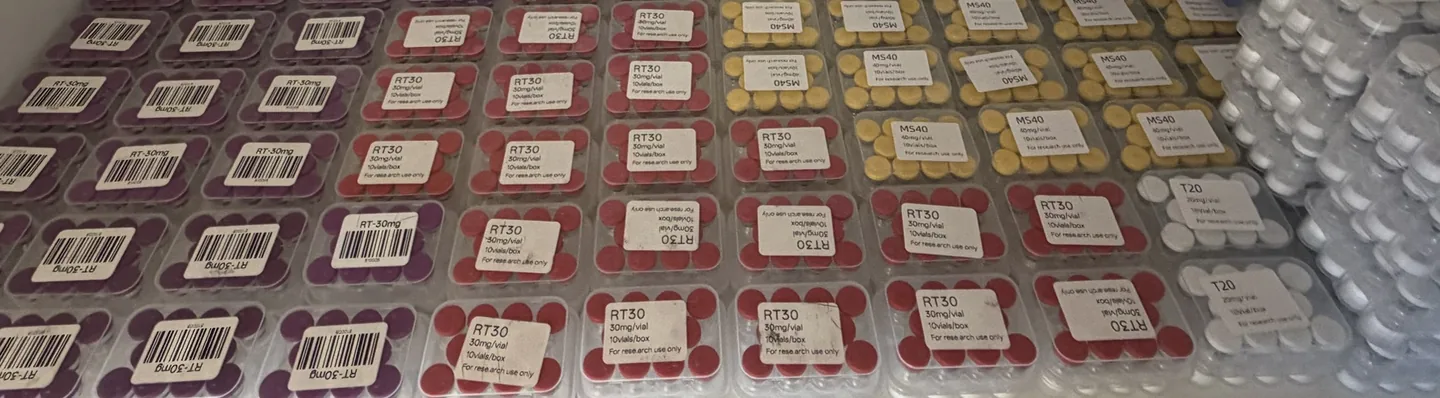 One shelf of stock: Retatrutide 30 mg in both label styles (purple caps, RT-30mg; red caps, RT30), MOTS-C 40 mg (yellow caps, MS40) and Tirzepatide 20 mg (white caps, T20), each in clear 10-vial cases